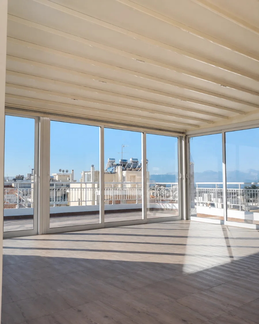 Verglaste Dachterrasse mit Schiebe-Glaselementen unter heller Beschattung und Blick über die Stadt