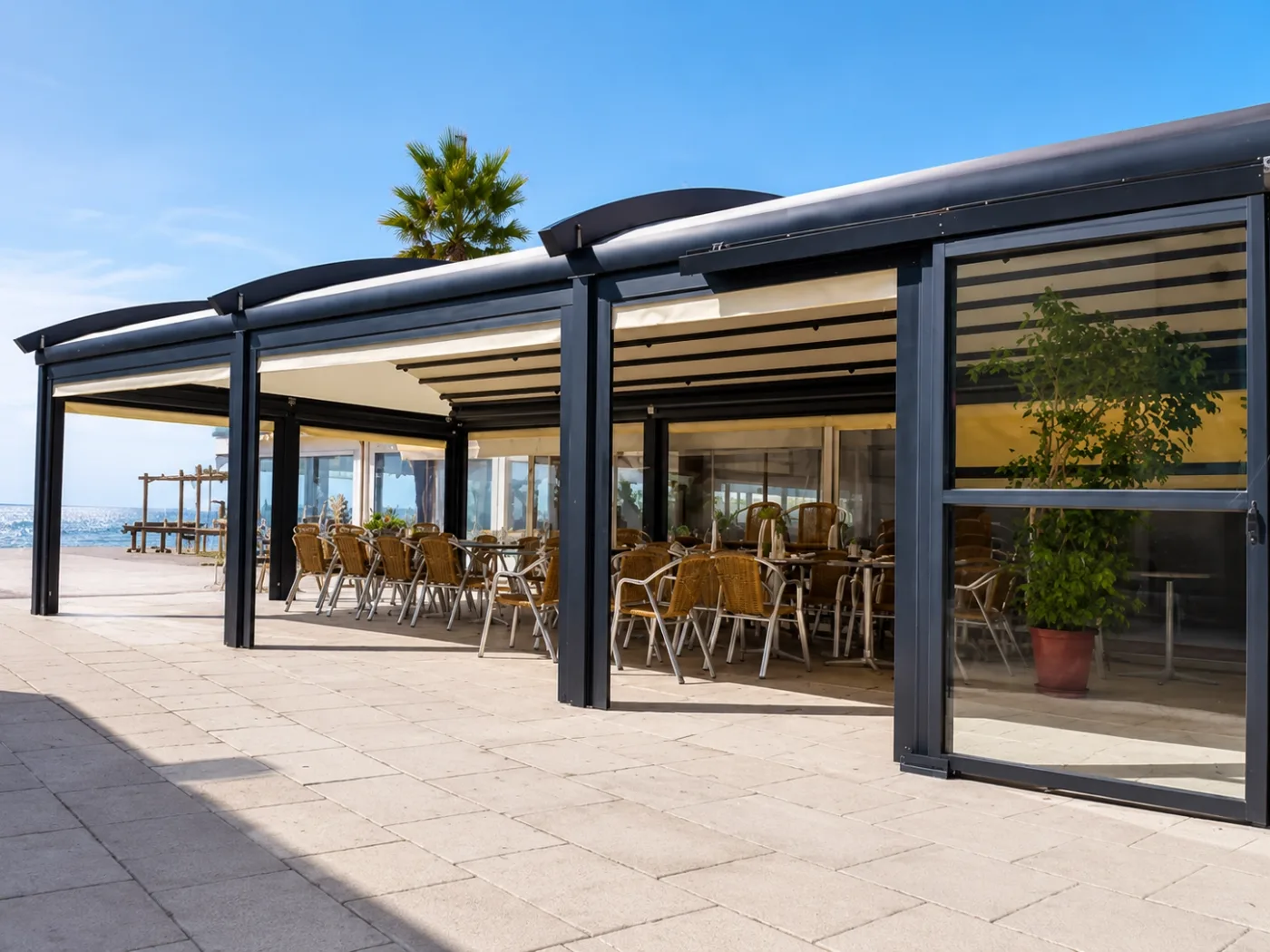 Gastronomieterrasse am Meer mit gebogenen Markisendächern und vertikalen Glasschiebeelementen