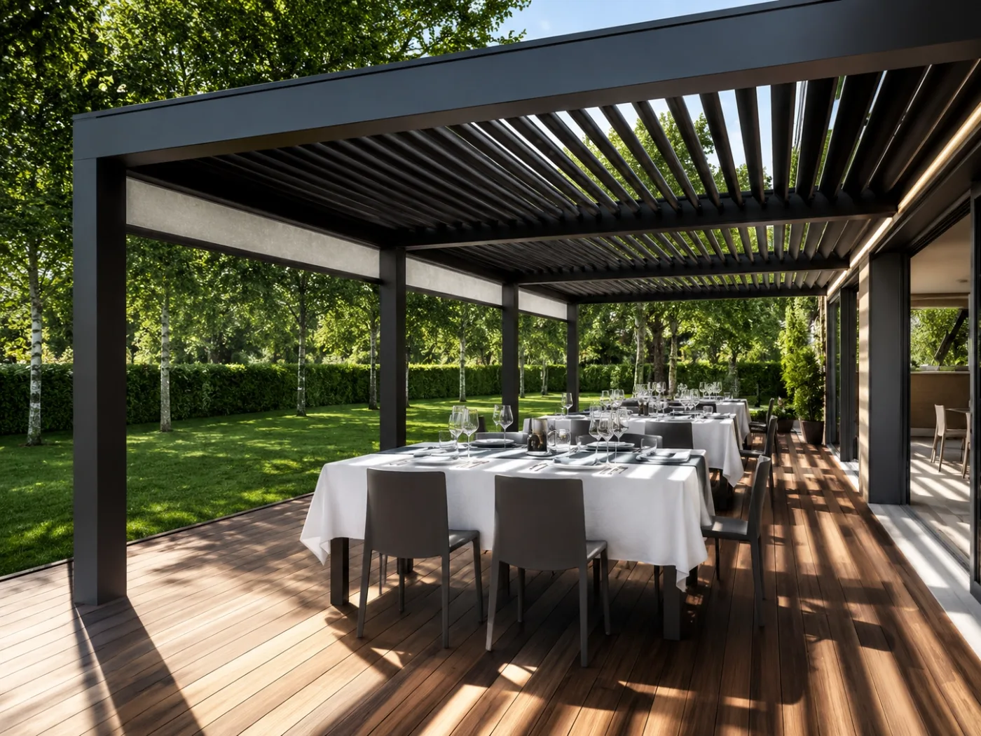 Anthrazitfarbenes Lamellendach über einer gedeckten Tafel auf einer Holzterrasse mit Blick in einen Garten