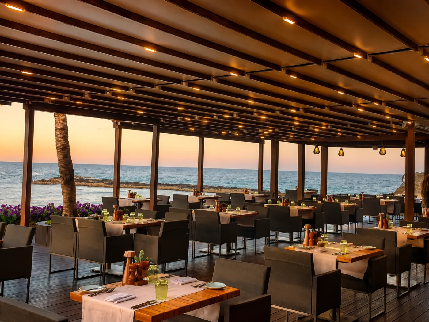 Restaurantterrasse am Meer unter einer beleuchteten Pergola im Abendlicht